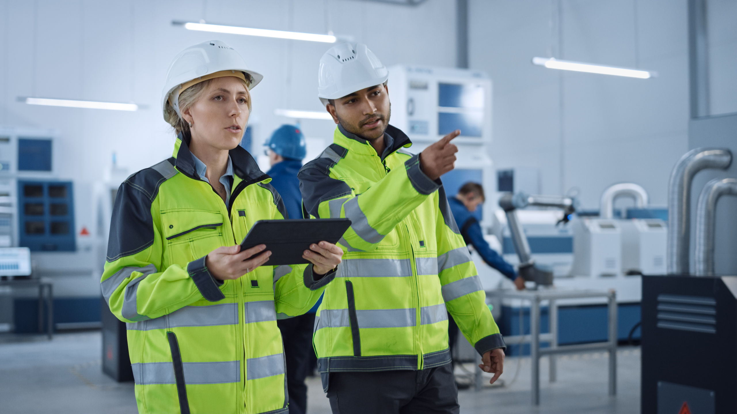 chief engineer and project supervisor in safety vests and hard hats walk through modern factory, talking, optimizing production. industrial facility: professionals use machinery.
