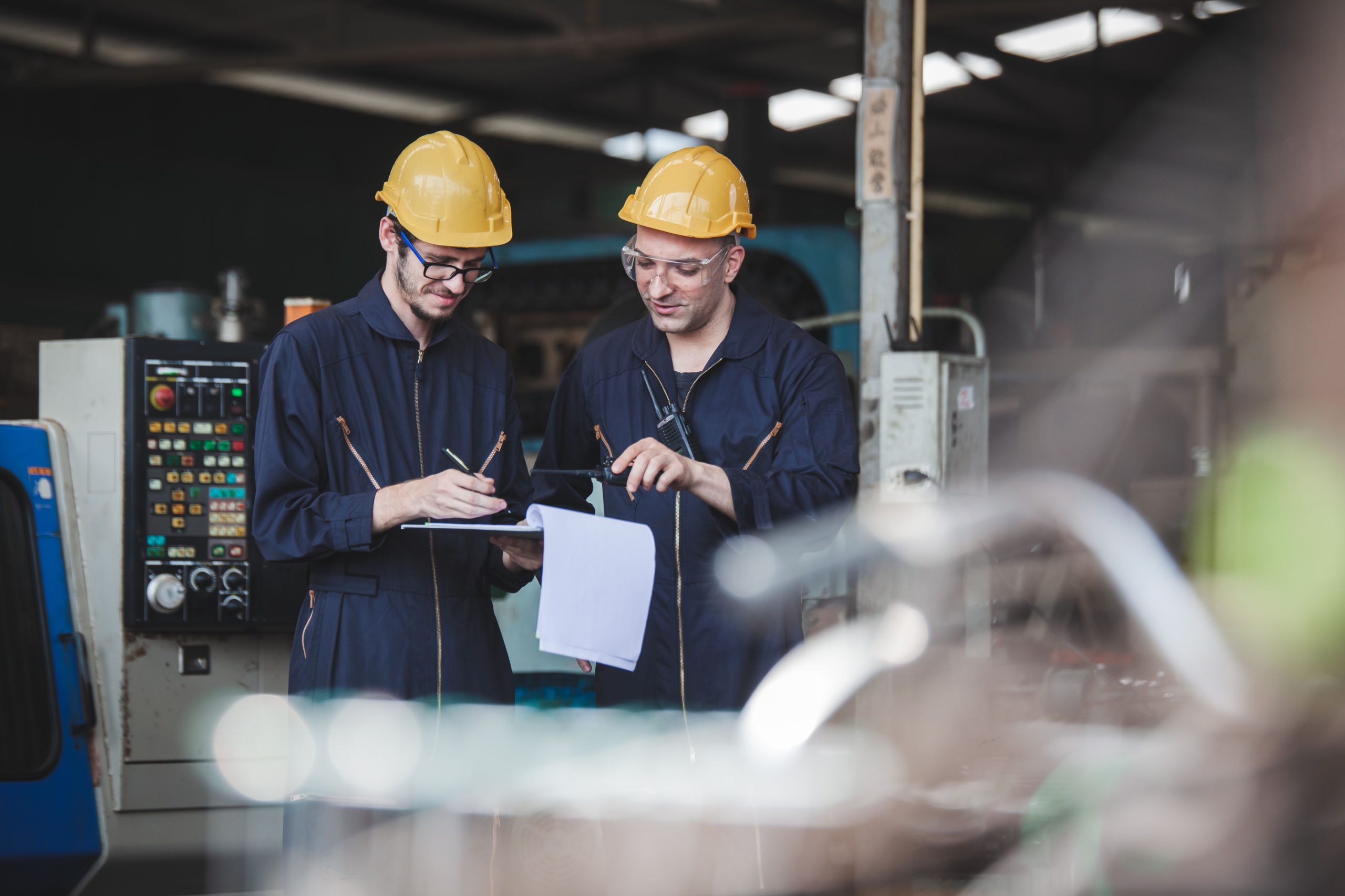 two workers at an industrial. technician engineer checking process on notebook to machinery in factory. workers using machine equipment in factory